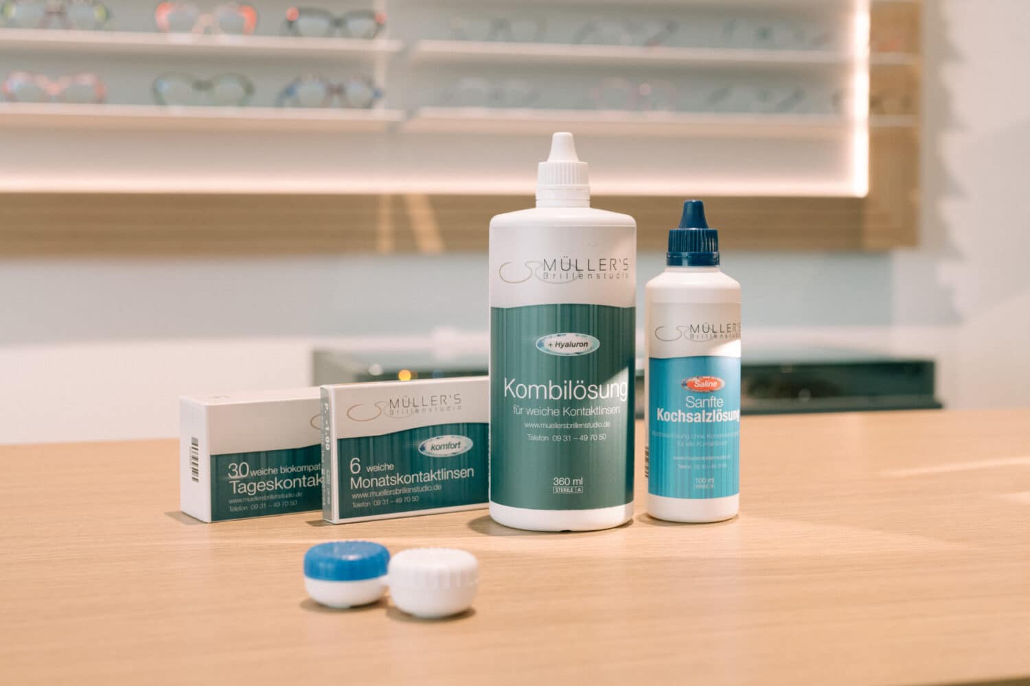 Kontaktlinsen-Pflegeprodukte von Müllers Brillenstudio – Kombilösung, Kochsalzlösung, Tages- und Monatskontaktlinsen auf Ladentheke.