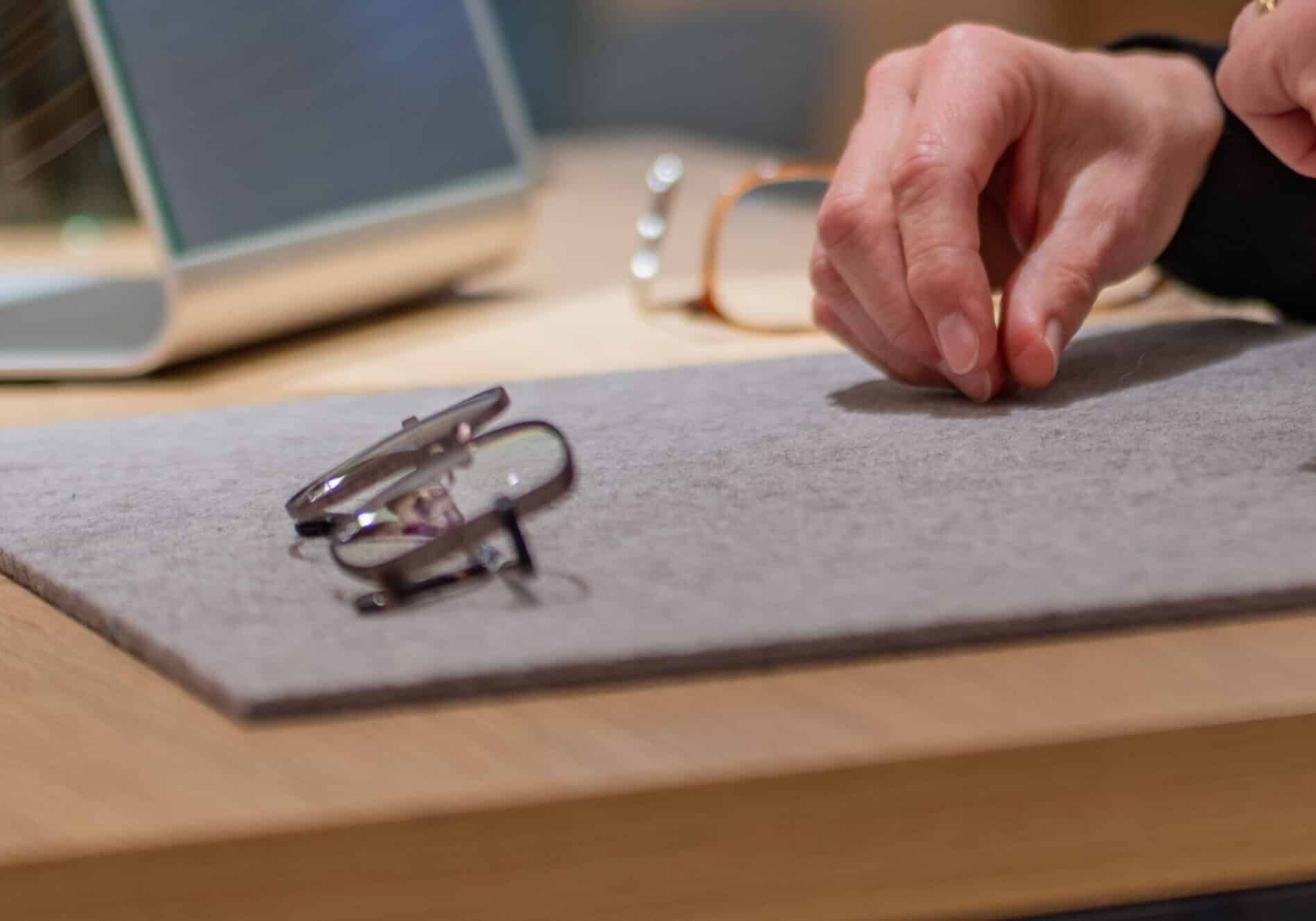 Optiker legt sorgfältig eine Brillenfassung auf eine Filzunterlage, um die Brille zu zeigen.