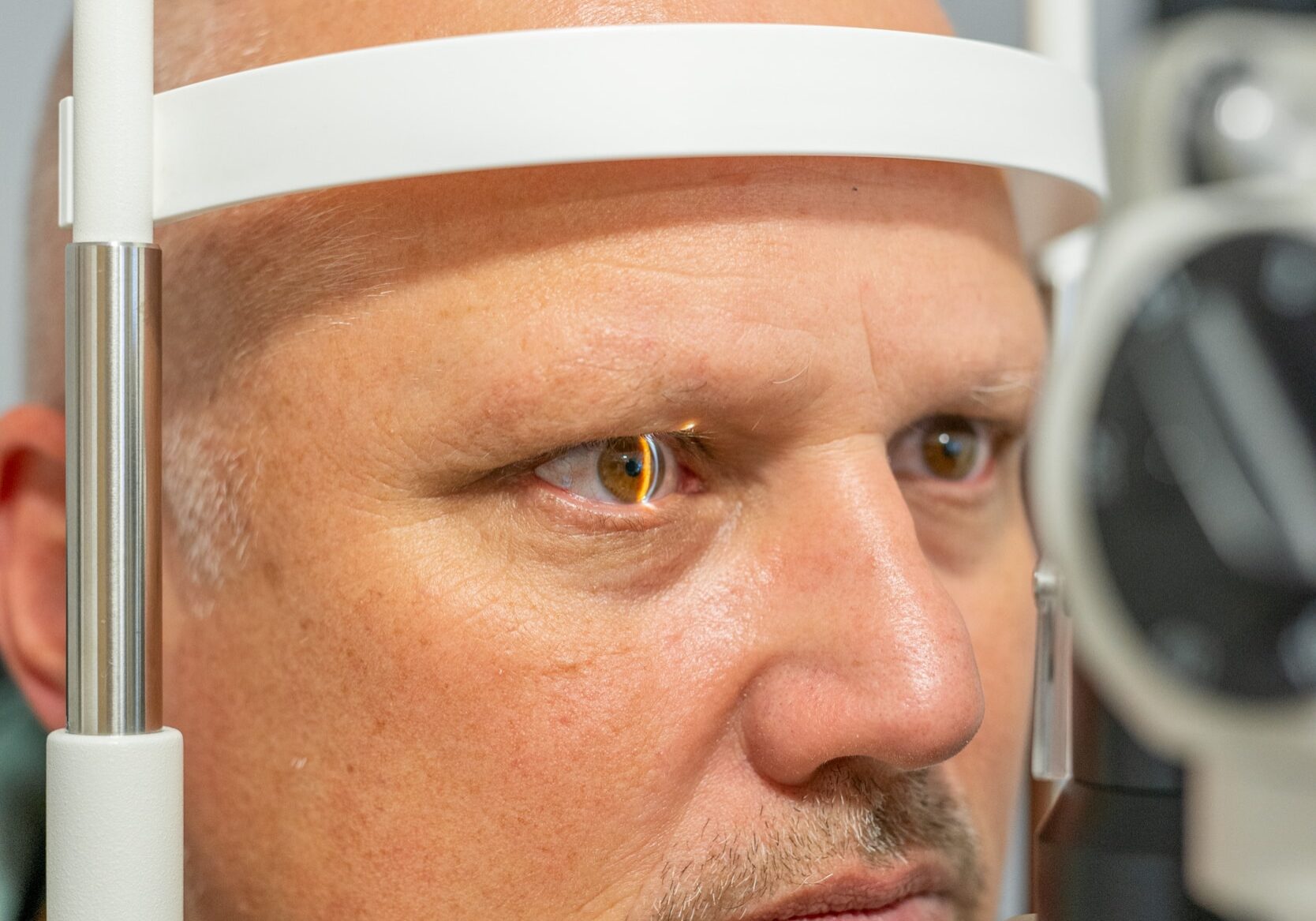 Mann mittleren Alters bei der optometrischen Augenuntersuchung an einer Spaltlampe beim Augenarzt.