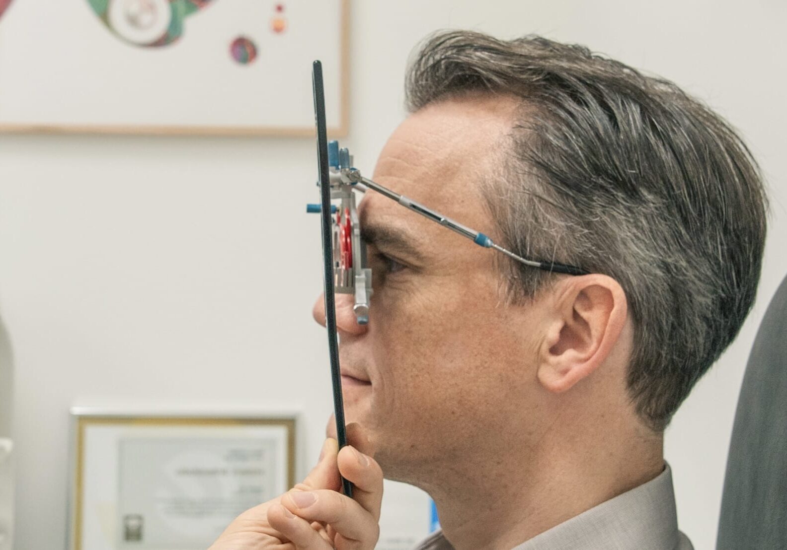 Optiker führt an einem Mann einem Sehtest durch und hält ihm ein Messgerät vor das Gesicht.